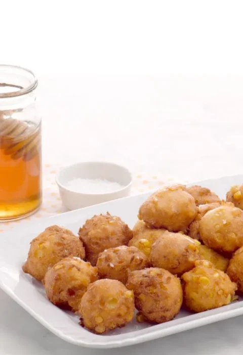 Golden brown Martha Stewart corn fritters piled on a plate with honey drizzle