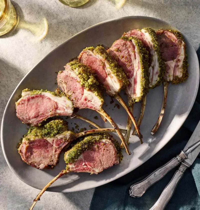 Herb-crusted roast rack of lamb with golden breadcrumb coating sliced between the bones on a serving plate