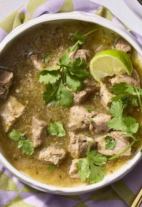 A bowl of martha stewart shortcut chile verde with fork-tender pork in green tomatillo sauce topped with fresh cilantro