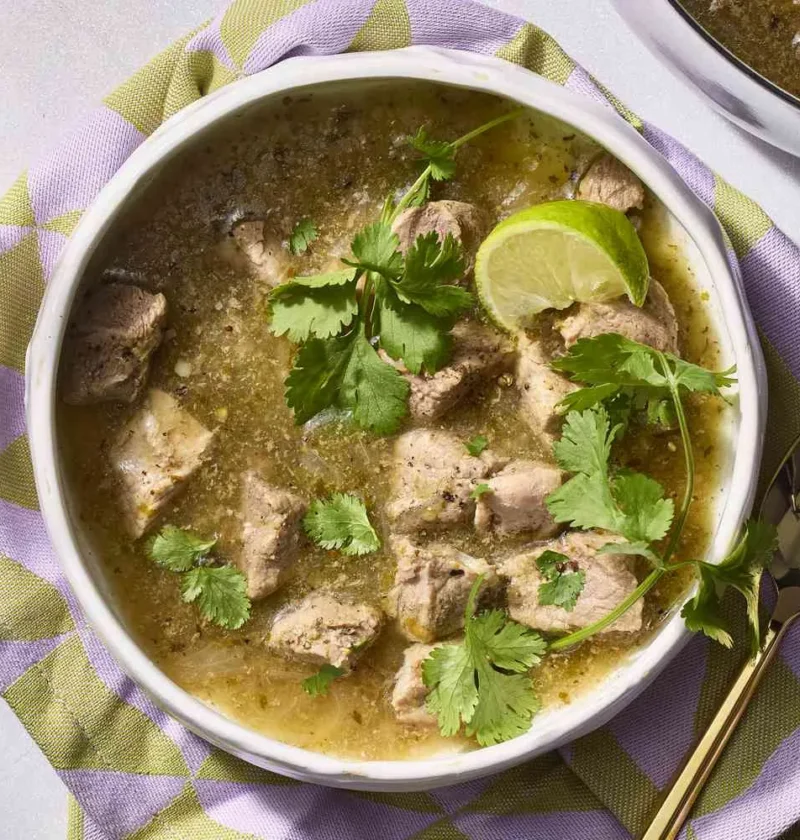 A bowl of martha stewart shortcut chile verde with fork-tender pork in green tomatillo sauce topped with fresh cilantro