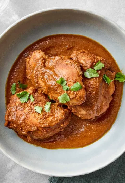 A plate of slow-cooker chicken mole with tender chicken thighs covered in dark, rich chocolate mole sauce