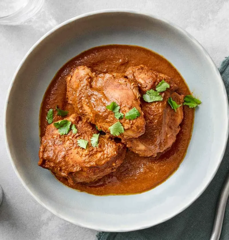 A plate of slow-cooker chicken mole with tender chicken thighs covered in dark, rich chocolate mole sauce