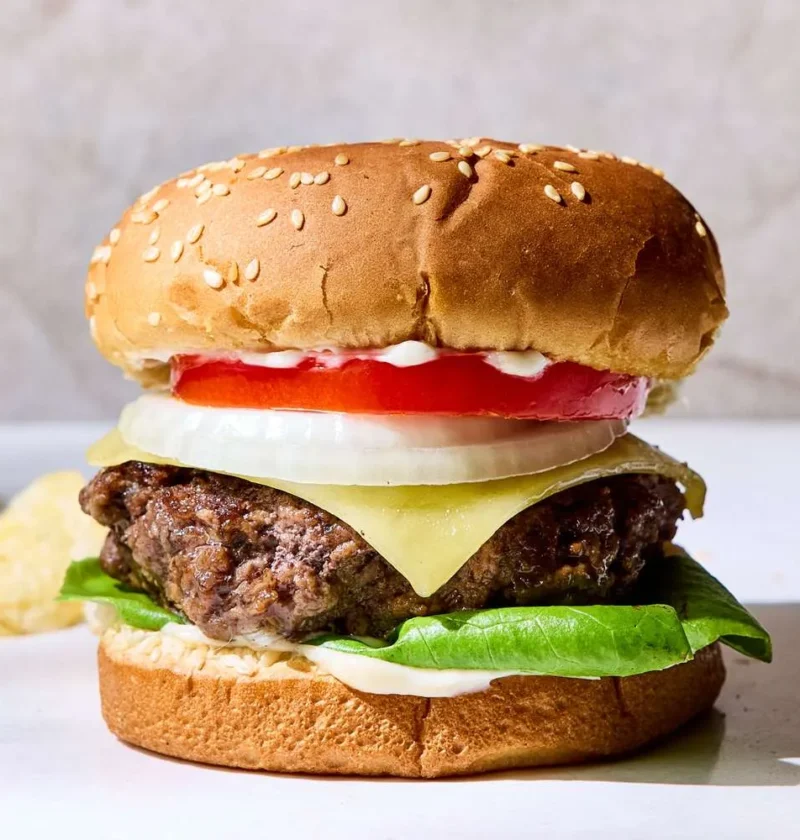 Thick grilled martha stewart thick burger with melted white cheddar, beefsteak tomato, and Vidalia onion on a toasted bakery roll