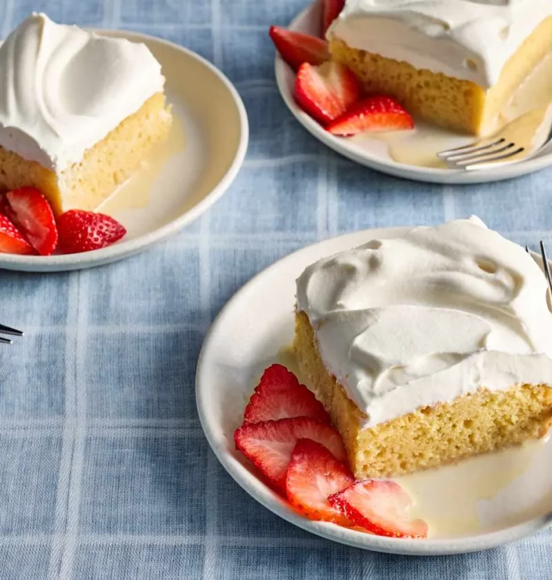 A slice of tres leches cake topped with whipped cream and fresh berries on a white plate