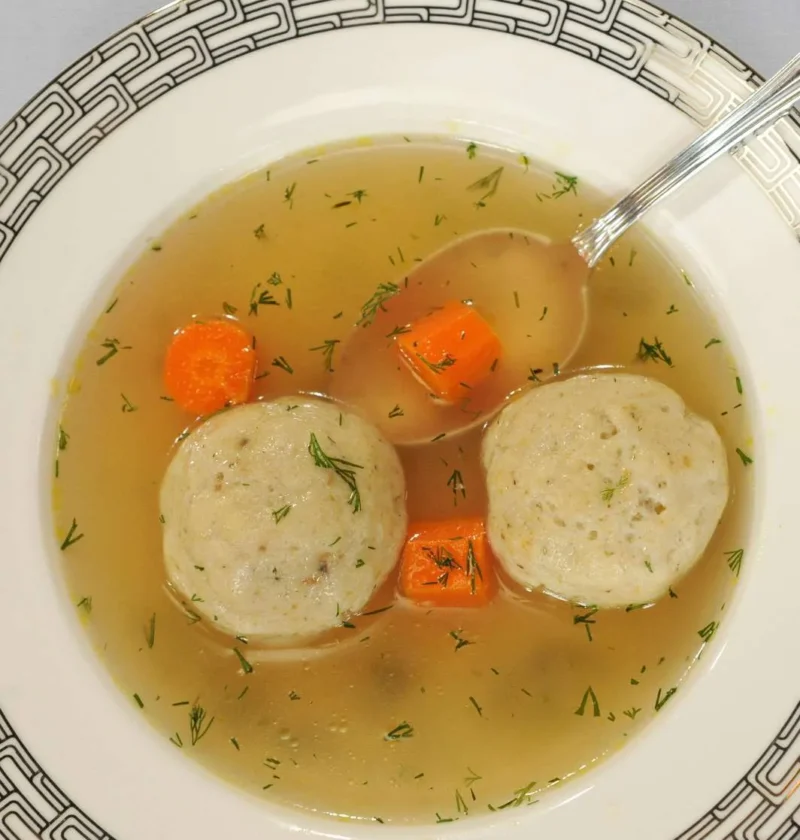 Bowl of vegetarian matzo ball soup with fluffy matzo balls floating in golden broth