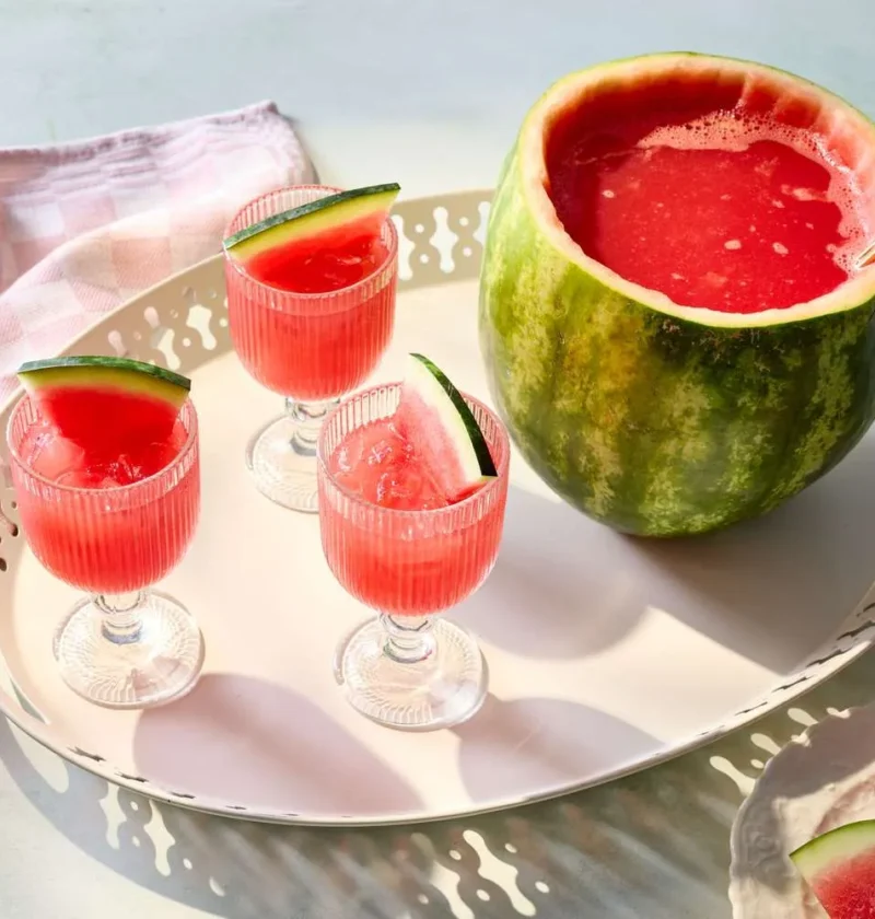 A hollowed out watermelon filled with fresh watermelon punch and seltzer, served over ice at a summer party