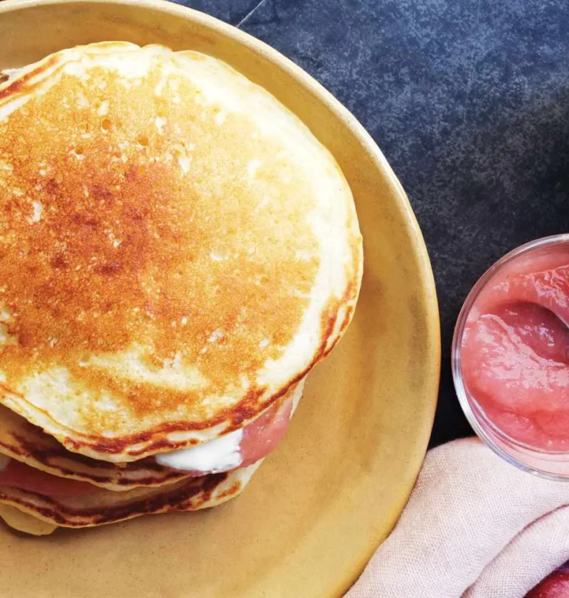 A stack of golden applesauce pancakes layered with sour cream and applesauce on a plate