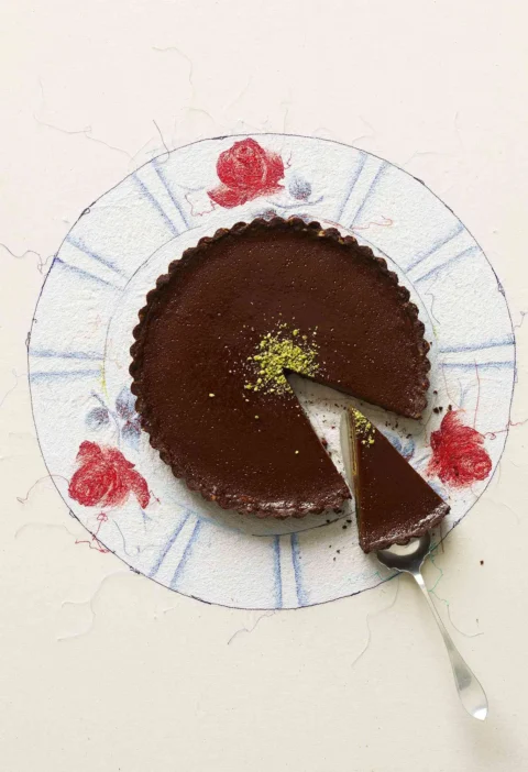 A slice of milk chocolate pistachio tart on a cocoa shortbread crust with bright green pistachios on top