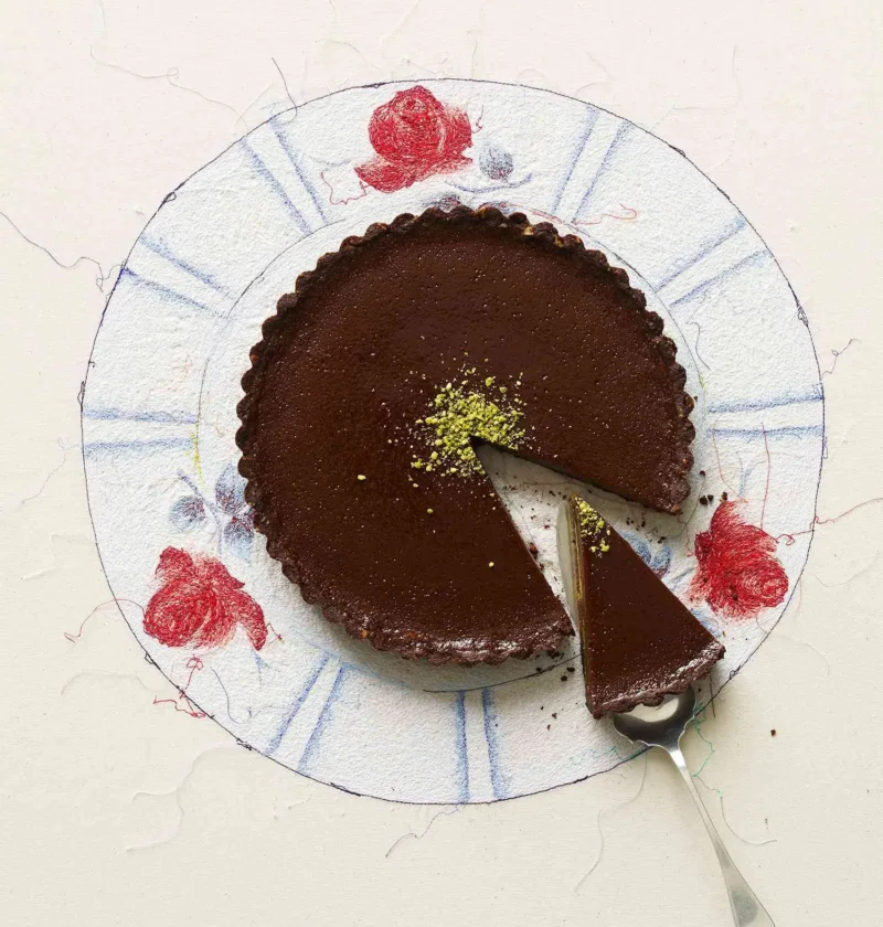 A slice of milk chocolate pistachio tart on a cocoa shortbread crust with bright green pistachios on top