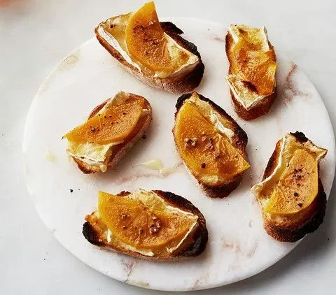 Persimmon and Brie crostini on a plate with caramelized brown sugar tops and cracked pepper