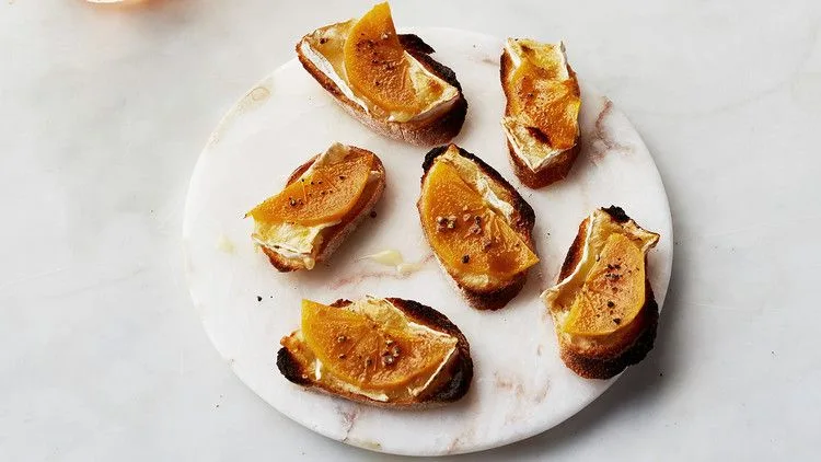 Persimmon and Brie crostini on a plate with caramelized brown sugar tops and cracked pepper