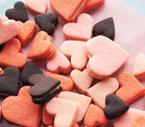 Pink heart sandwich cookies in three sizes and shades of pink arranged on a white surface
