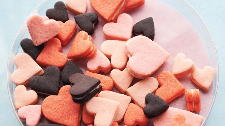 Pink heart sandwich cookies in three sizes and shades of pink arranged on a white surface