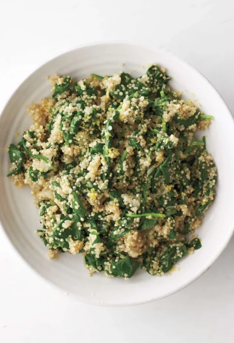 A bowl of quinoa and spinach pilaf with bright lemon zest and wilted baby greens