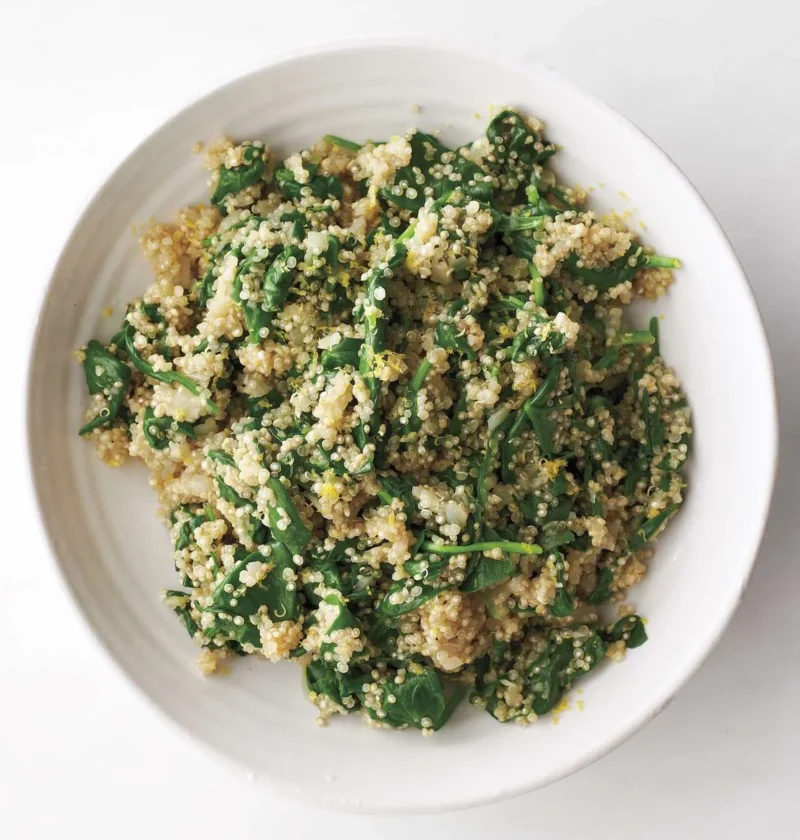 A bowl of quinoa and spinach pilaf with bright lemon zest and wilted baby greens