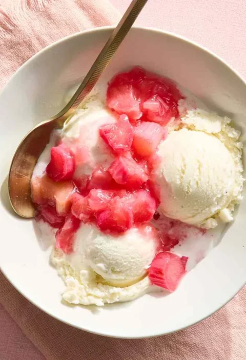 A bowl of chunky rhubarb compote with visible pink and green pieces in a rosy sauce