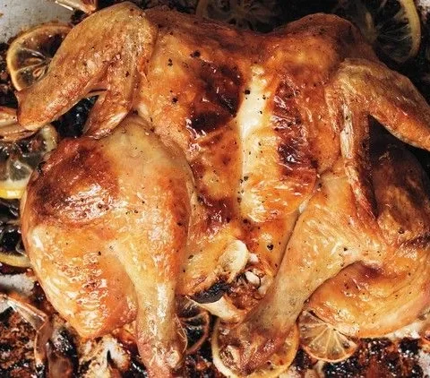 Roast spatchcocked lemon chicken on a sheet pan with golden skin, roasted lemon slices, and caramelized shallots