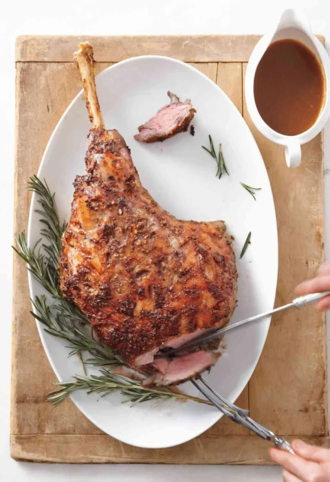 Roasted leg of lamb with red wine gravy on a serving platter, sliced to show the rosy interior with a crisp rosemary crust