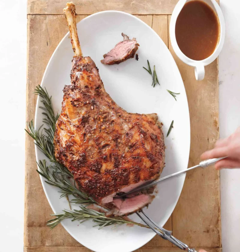 Roasted leg of lamb with red wine gravy on a serving platter, sliced to show the rosy interior with a crisp rosemary crust