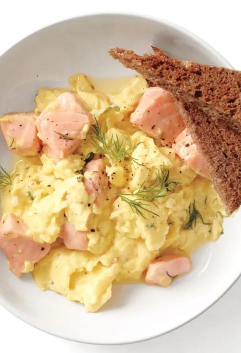 Creamy salmon and scrambled eggs with fresh dill served on a plate with toast