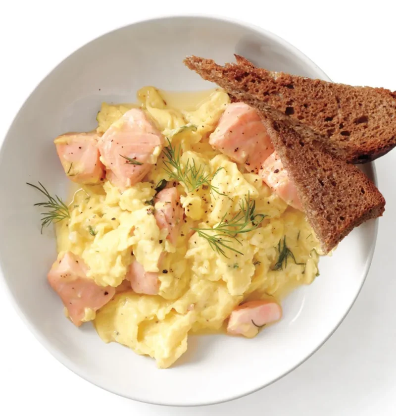 Creamy salmon and scrambled eggs with fresh dill served on a plate with toast