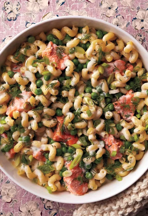A baked salmon noodle casserole with cavatappi pasta, chunks of pink salmon, bright green peas, and fresh dill in a golden baking dish