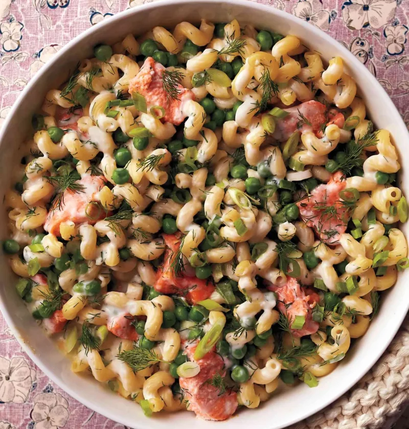 A baked salmon noodle casserole with cavatappi pasta, chunks of pink salmon, bright green peas, and fresh dill in a golden baking dish