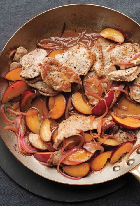 Sautéed pork tenderloin slices with caramelized plum wedges and red onion in a skillet