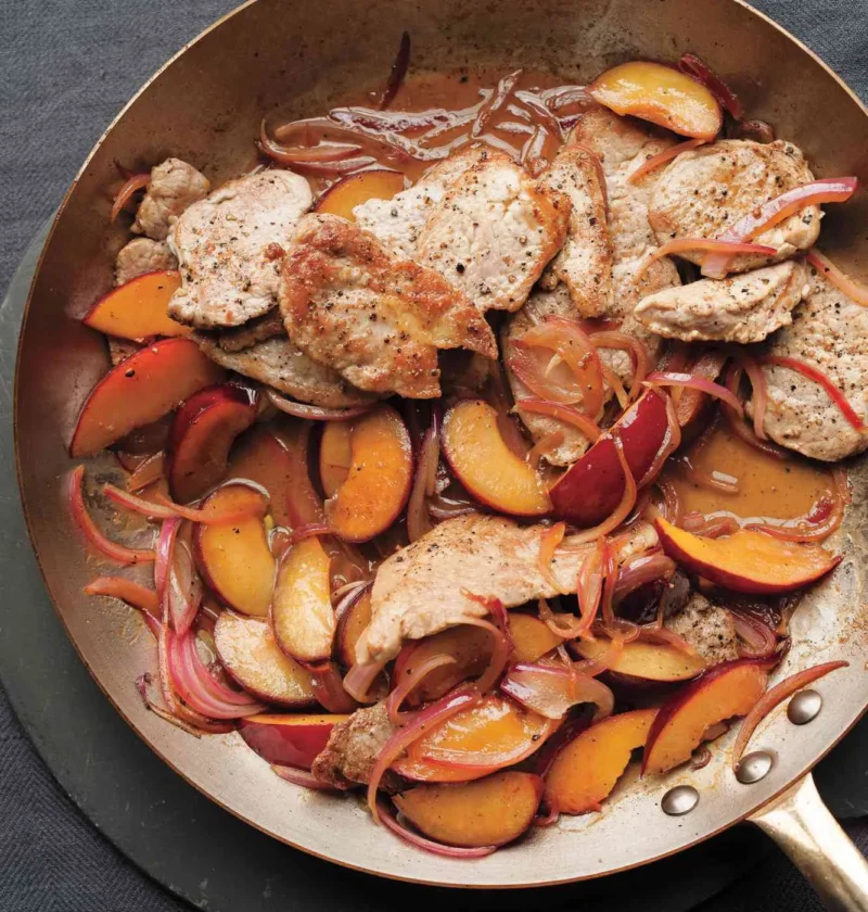 Sautéed pork tenderloin slices with caramelized plum wedges and red onion in a skillet