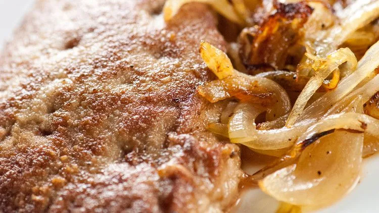 Martha Stewart sauteed calf liver browned in butter with sage and topped with caramelized onions on a white plate
