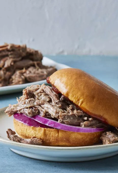 Shredded beef chuck roast in a bowl with two forks for pulling, a Martha Stewart slow cooker dinner