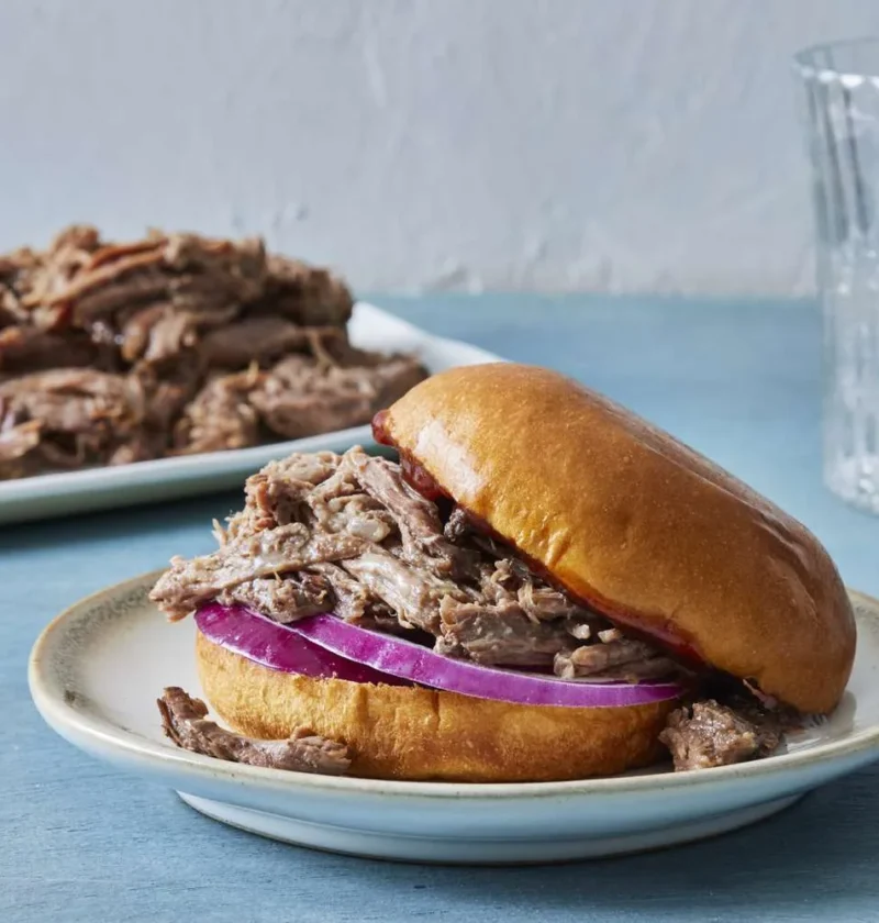 Shredded beef chuck roast in a bowl with two forks for pulling, a Martha Stewart slow cooker dinner