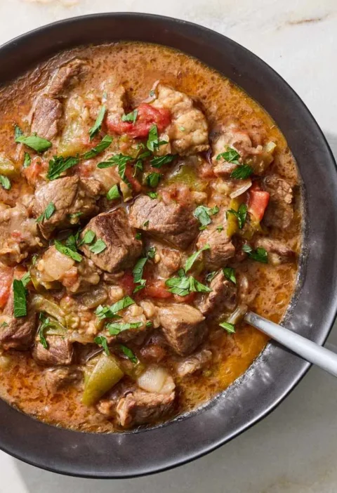 Slow-cooker carne guisada with tender beef chunks in a rich cumin-spiced tomato gravy, served in a bowl