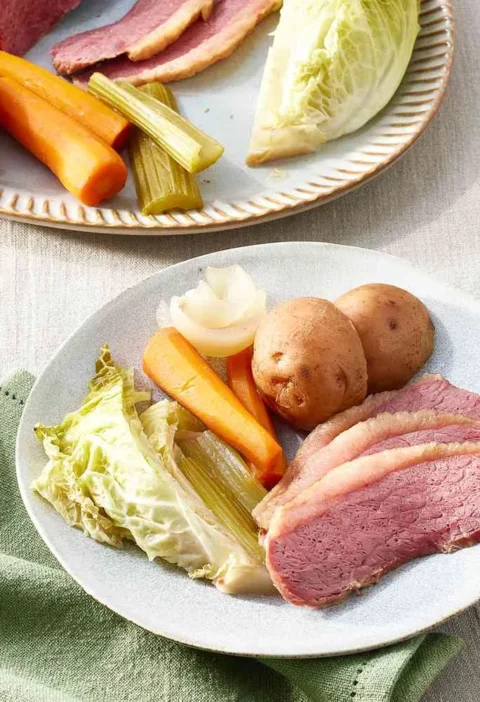 Slow-cooker corned beef and cabbage sliced against the grain on a platter with carrots, potatoes, and Savoy cabbage wedges