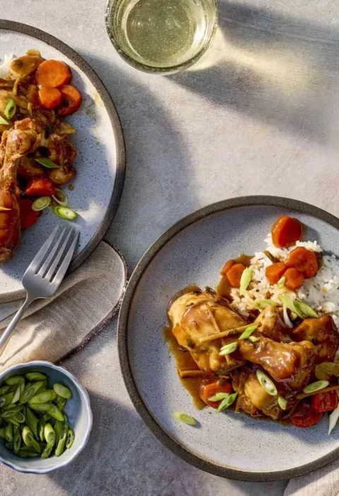 Slow cooker soy-ginger chicken drumsticks and thighs in a glossy brown sauce with carrots, scallions, and cilantro served over white rice