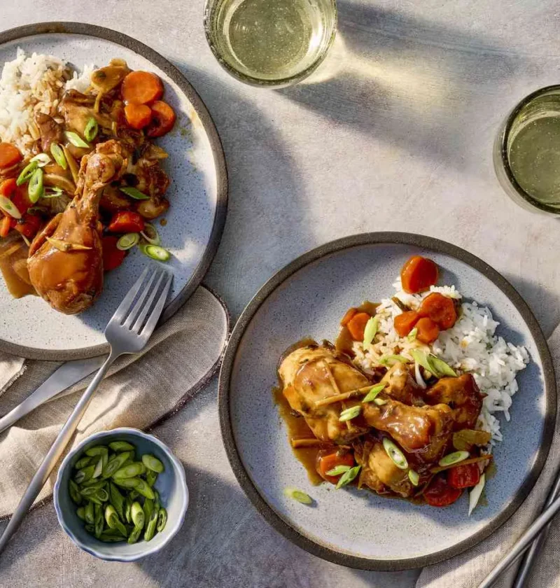 Slow cooker soy-ginger chicken drumsticks and thighs in a glossy brown sauce with carrots, scallions, and cilantro served over white rice