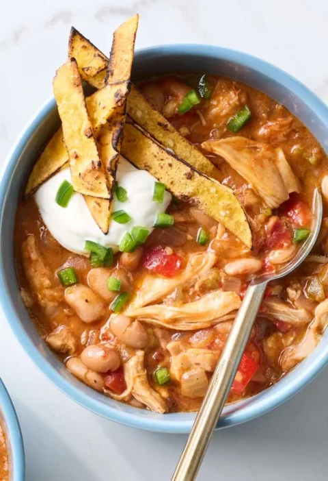Slow-cooker Tex-Mex chicken and beans topped with sour cream, jalapeno, and tortilla chips in a white bowl
