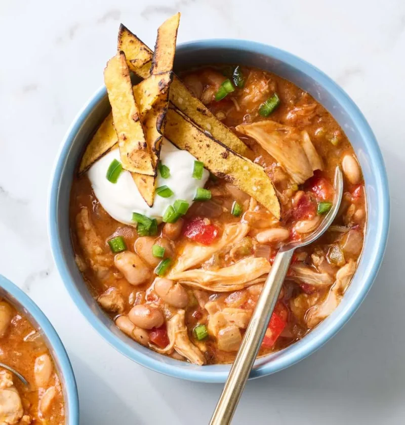 Slow-cooker Tex-Mex chicken and beans topped with sour cream, jalapeno, and tortilla chips in a white bowl