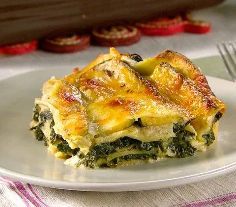 A baking dish of Martha Stewart spinach lasagna with golden bubbling mozzarella on top and layers of spinach and bechamel visible at the edges