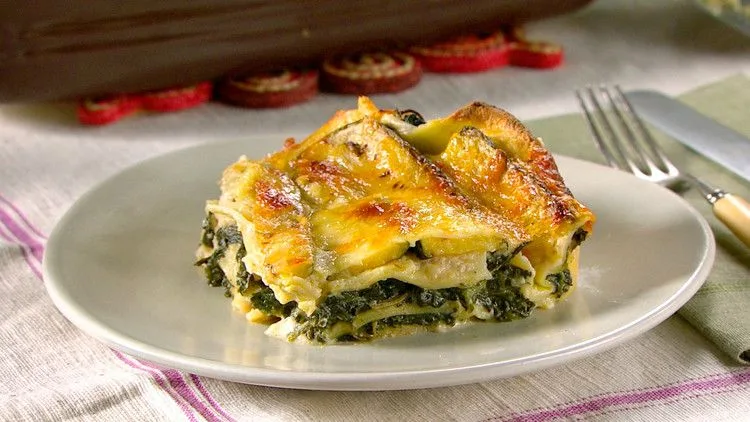 A baking dish of Martha Stewart spinach lasagna with golden bubbling mozzarella on top and layers of spinach and bechamel visible at the edges