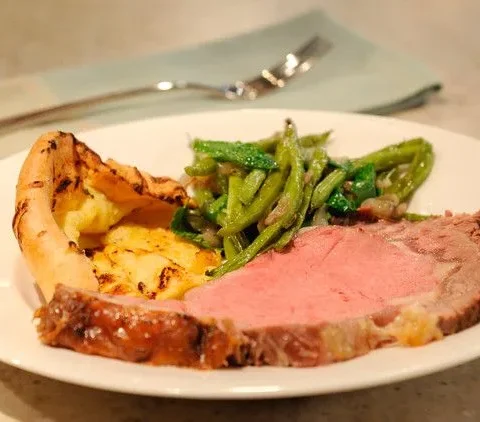 Standing rib roast prime rib with a dry mustard and rosemary crust sliced on a carving board with Yorkshire pudding