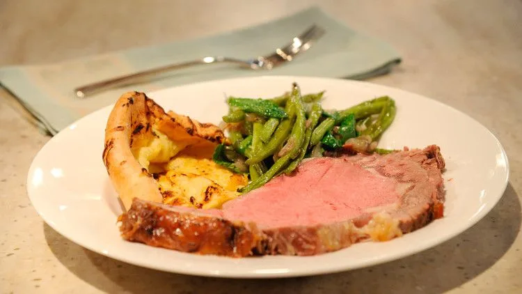 Standing rib roast prime rib with a dry mustard and rosemary crust sliced on a carving board with Yorkshire pudding
