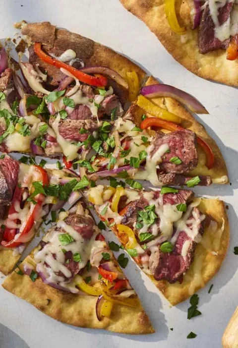 Steak pizza with peppers and onions topped with melted Monterey Jack cheese on golden crust