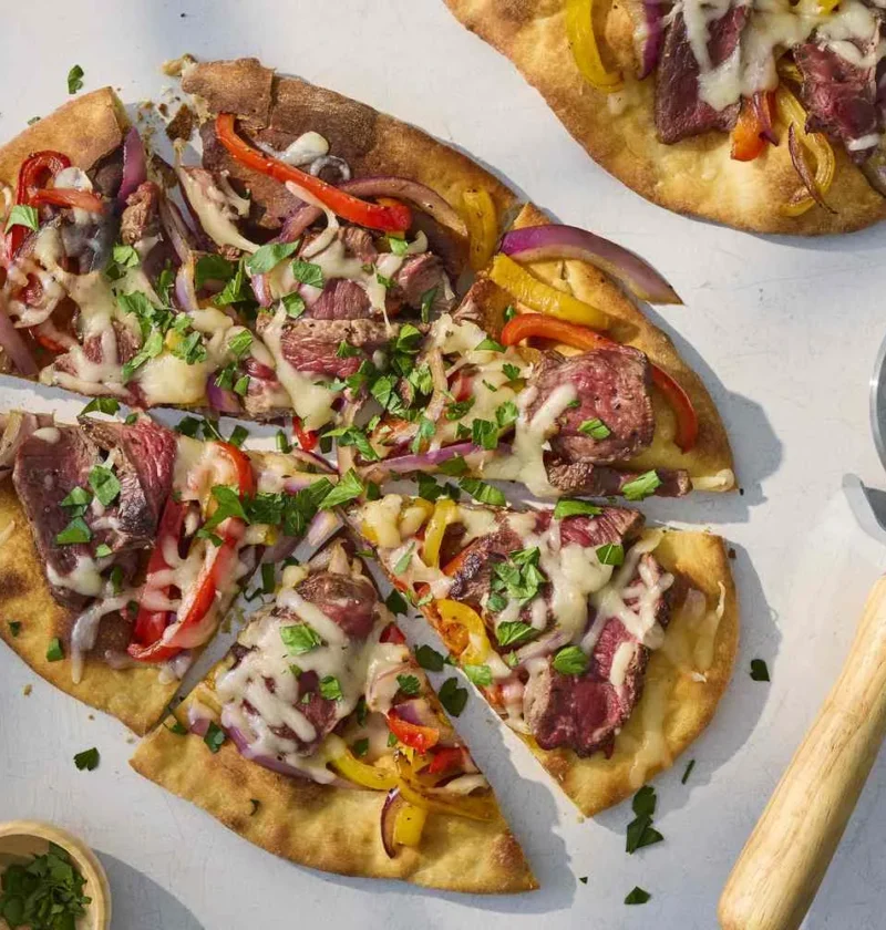 Steak pizza with peppers and onions topped with melted Monterey Jack cheese on golden crust