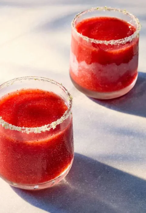 Frozen strawberry daiquiri in a glass with a lime sugar rim and fresh strawberries