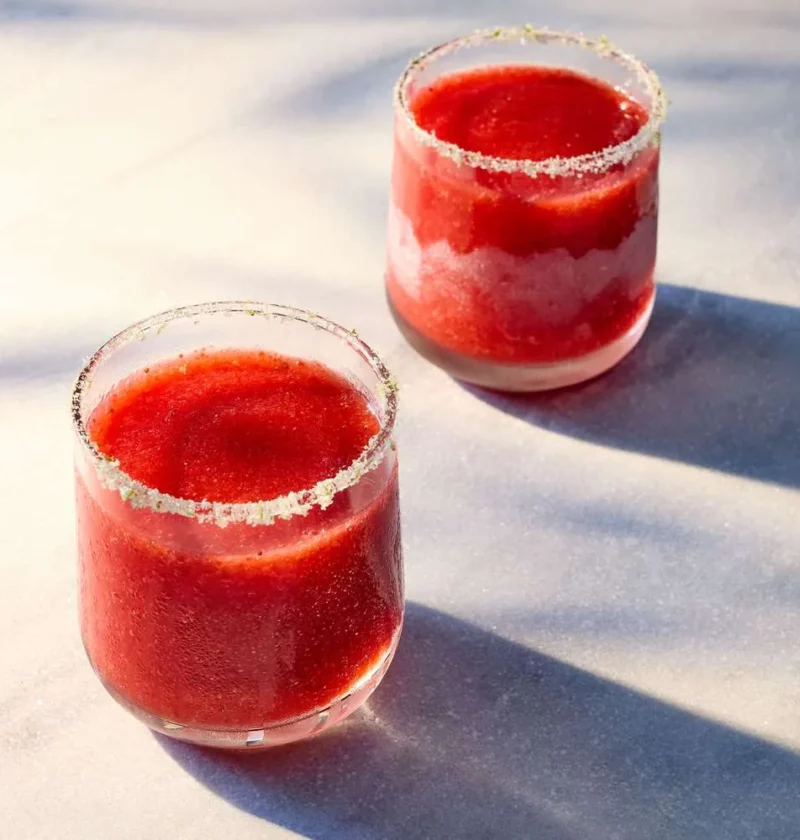 Frozen strawberry daiquiri in a glass with a lime sugar rim and fresh strawberries