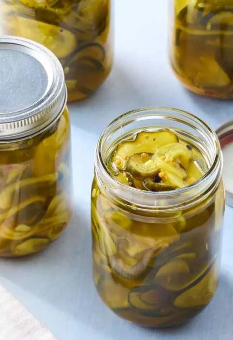 Jars of sweet and spicy bread-and-butter pickles with Kirby cucumber rounds in golden brine