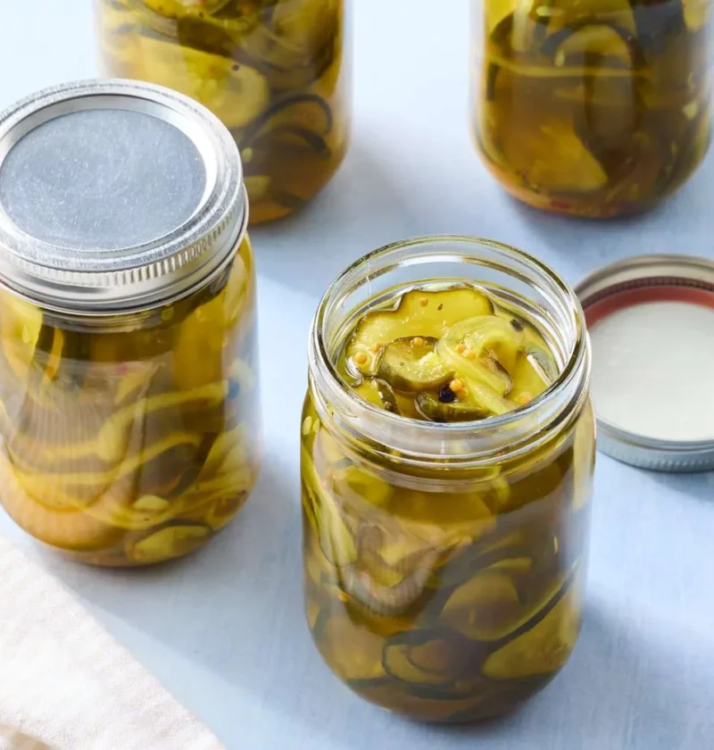 Jars of sweet and spicy bread-and-butter pickles with Kirby cucumber rounds in golden brine