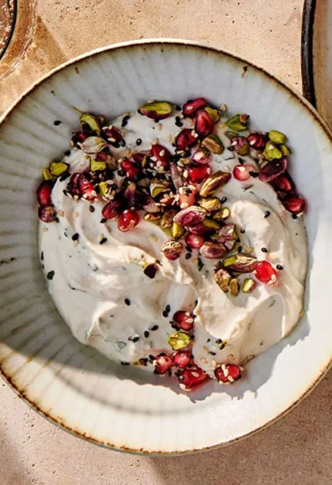 A bowl of creamy tahini-yogurt dip topped with pomegranate arils, toasted pine nuts, and sesame seeds