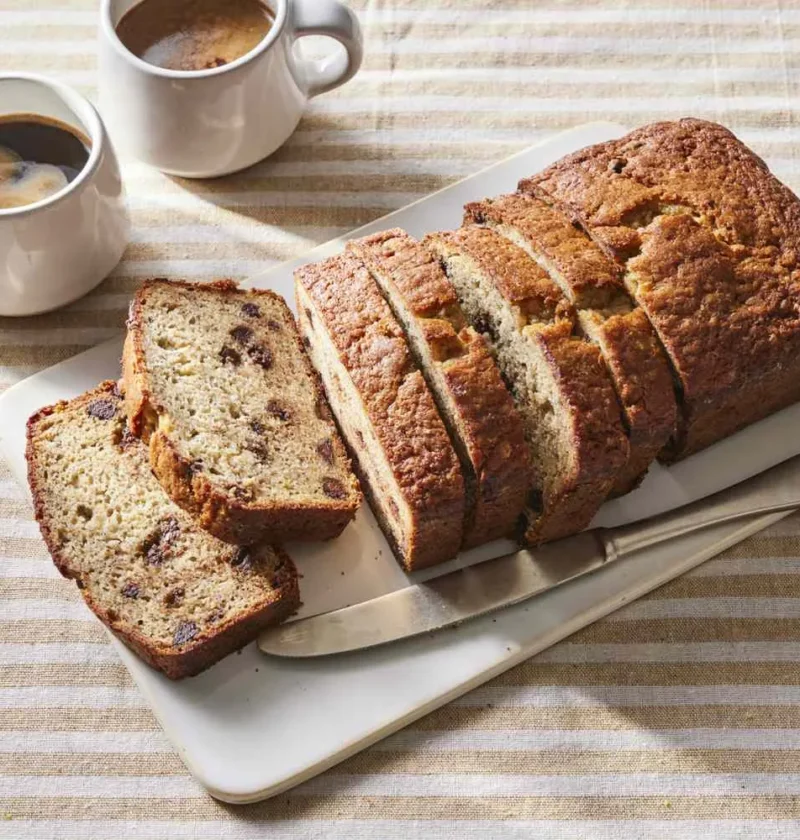 Sliced banana chocolate chip bread with melted semisweet chocolate and golden crust on a cutting board